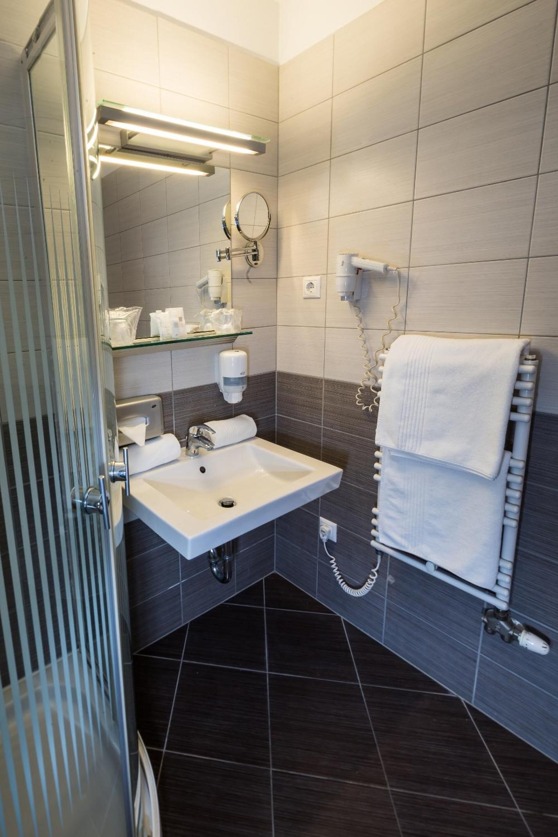 A modern bathroom with a white sink, a glass shelf with toiletries, a towel rack, and a mirror.