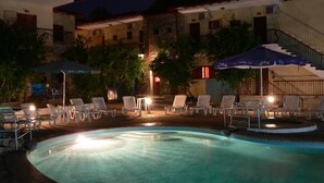 A swimming pool with lounge chairs and umbrellas, surrounded by buildings with balconies and air conditioning units.
