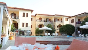 An outdoor dining area with tables set for a meal, a pool, and a building with multiple balconies and a stone facade.