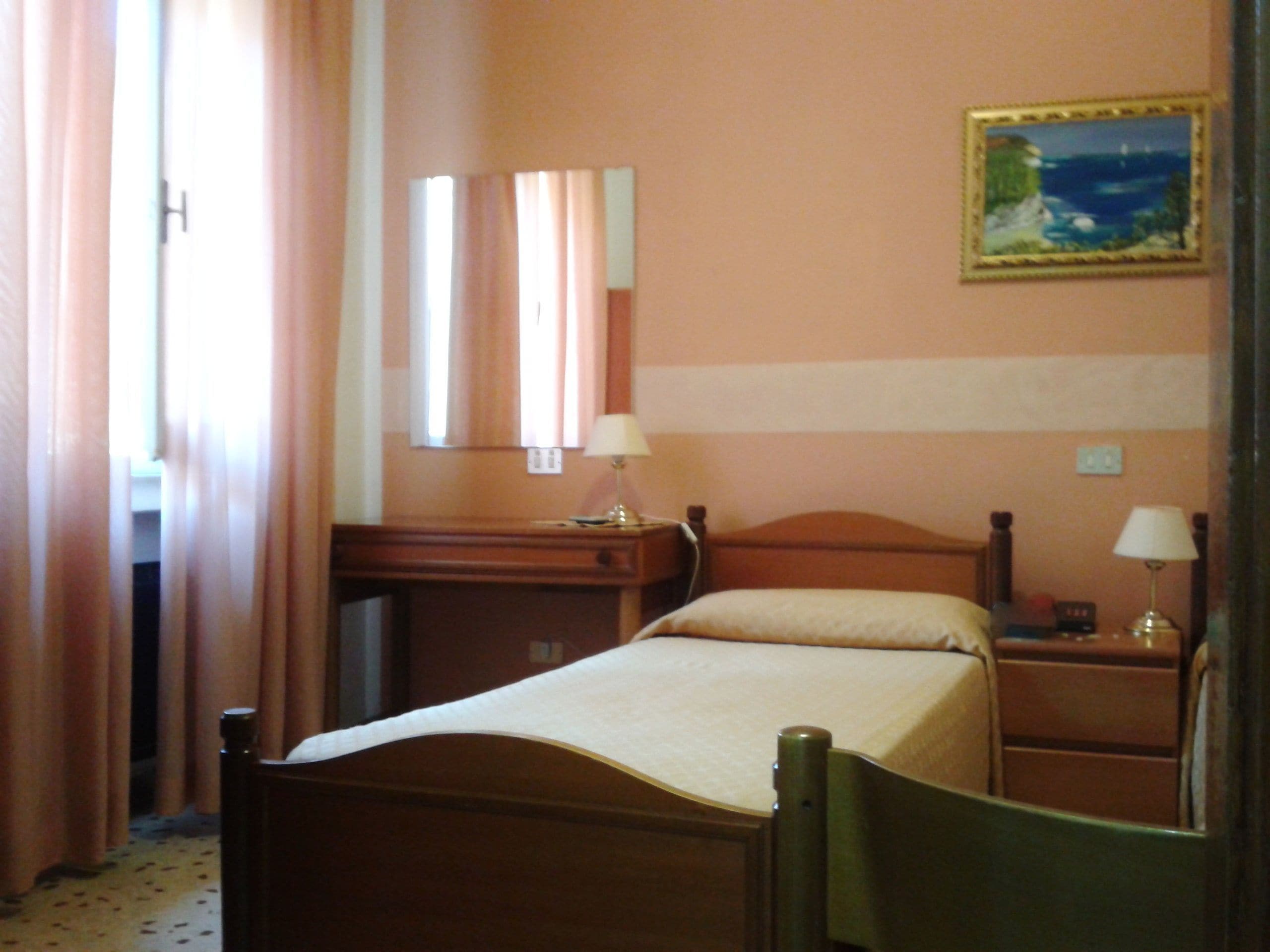 Una habitación de hotel con cama, escritorio, silla, mesita de noche y un cuadro en la pared.
