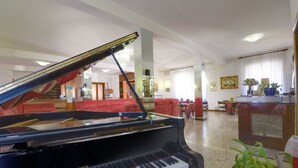 A grand piano in a spacious living area with red sofas, a dining table, and a bar area. - San Gabriele (Loreto)
