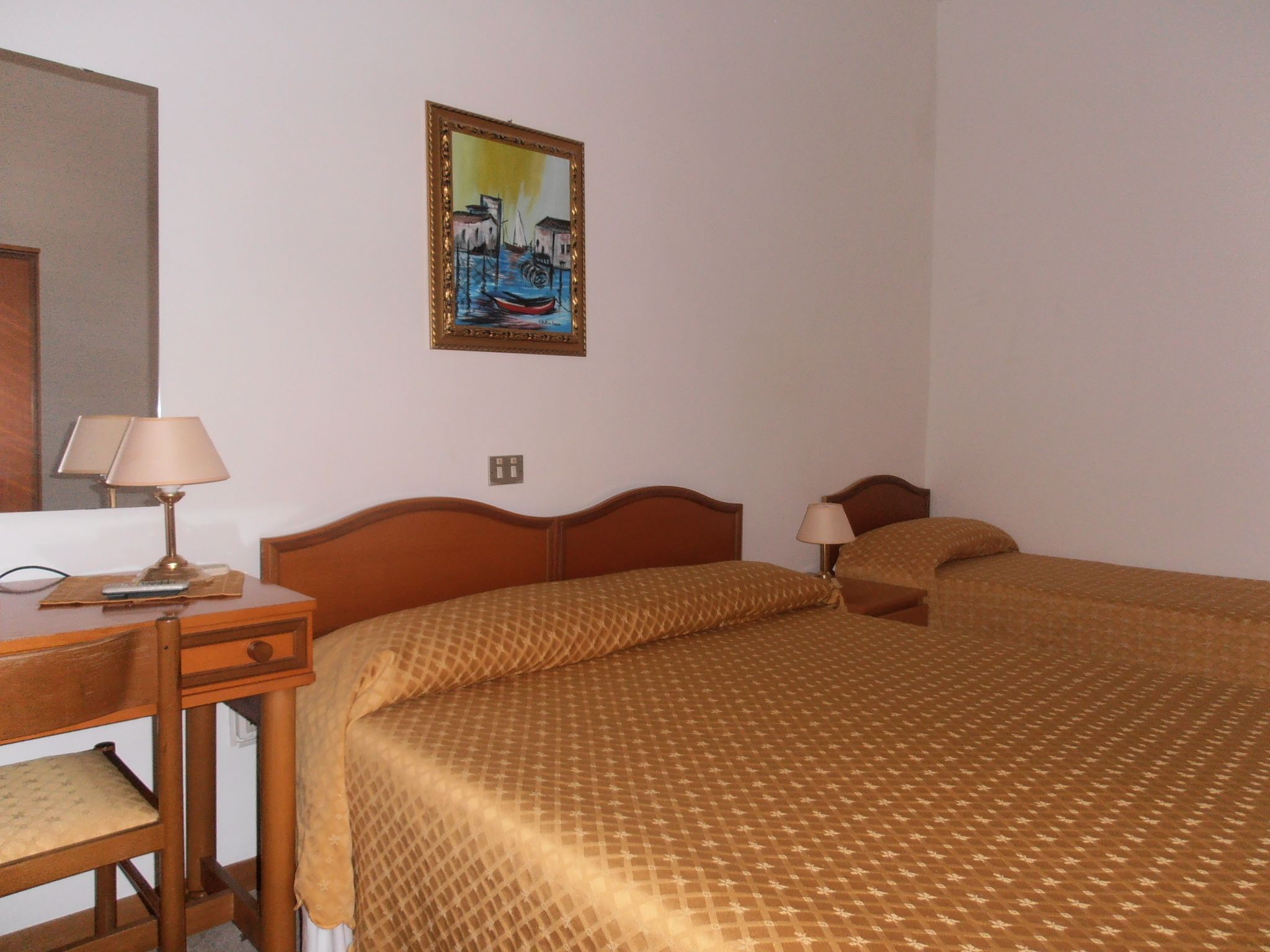 Une chambre d’hôtel avec deux lits, un bureau avec une lampe et un tableau au mur.