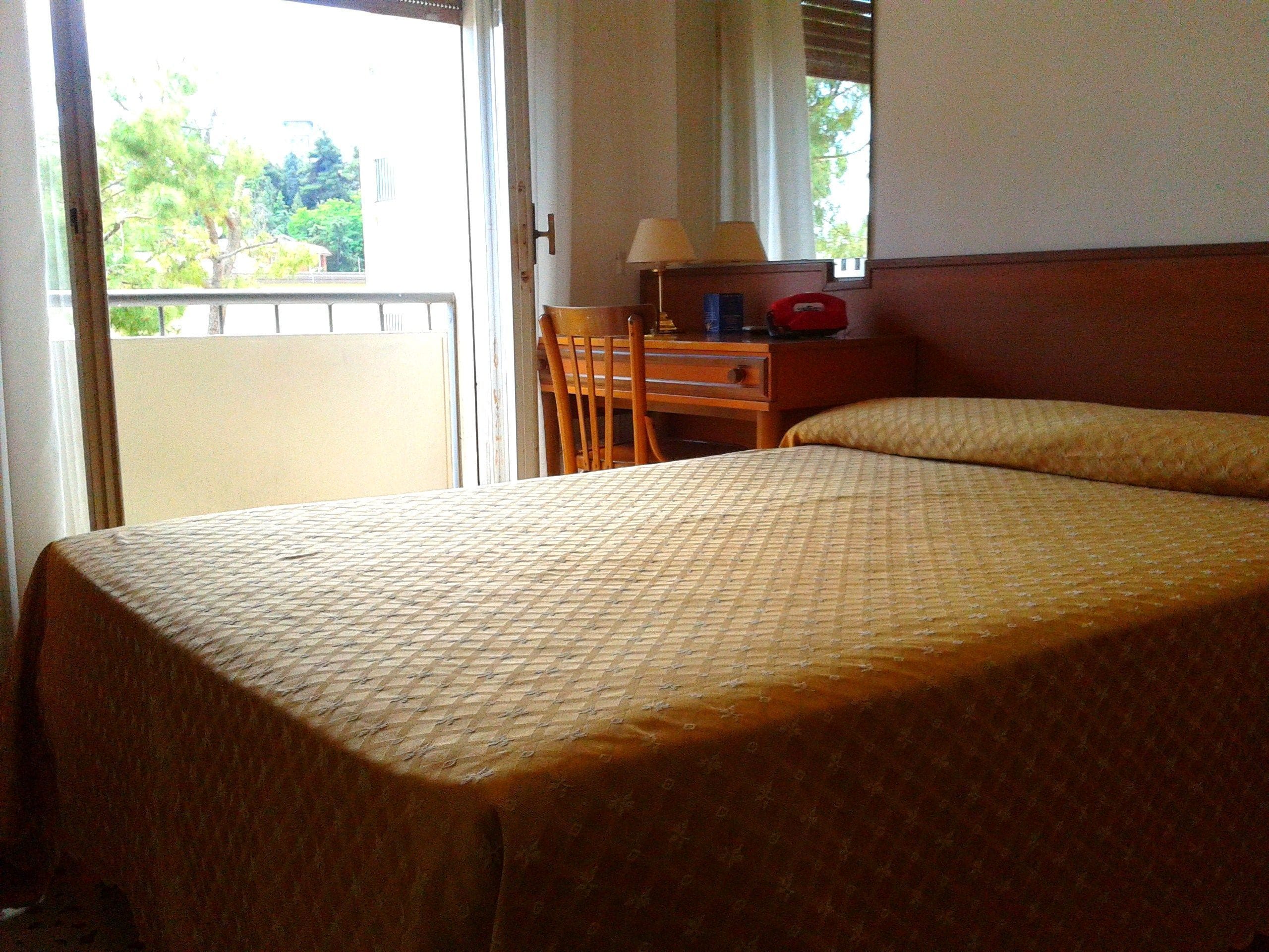 Habitación de hotel con cama, escritorio, silla y ventana con vista a follaje.