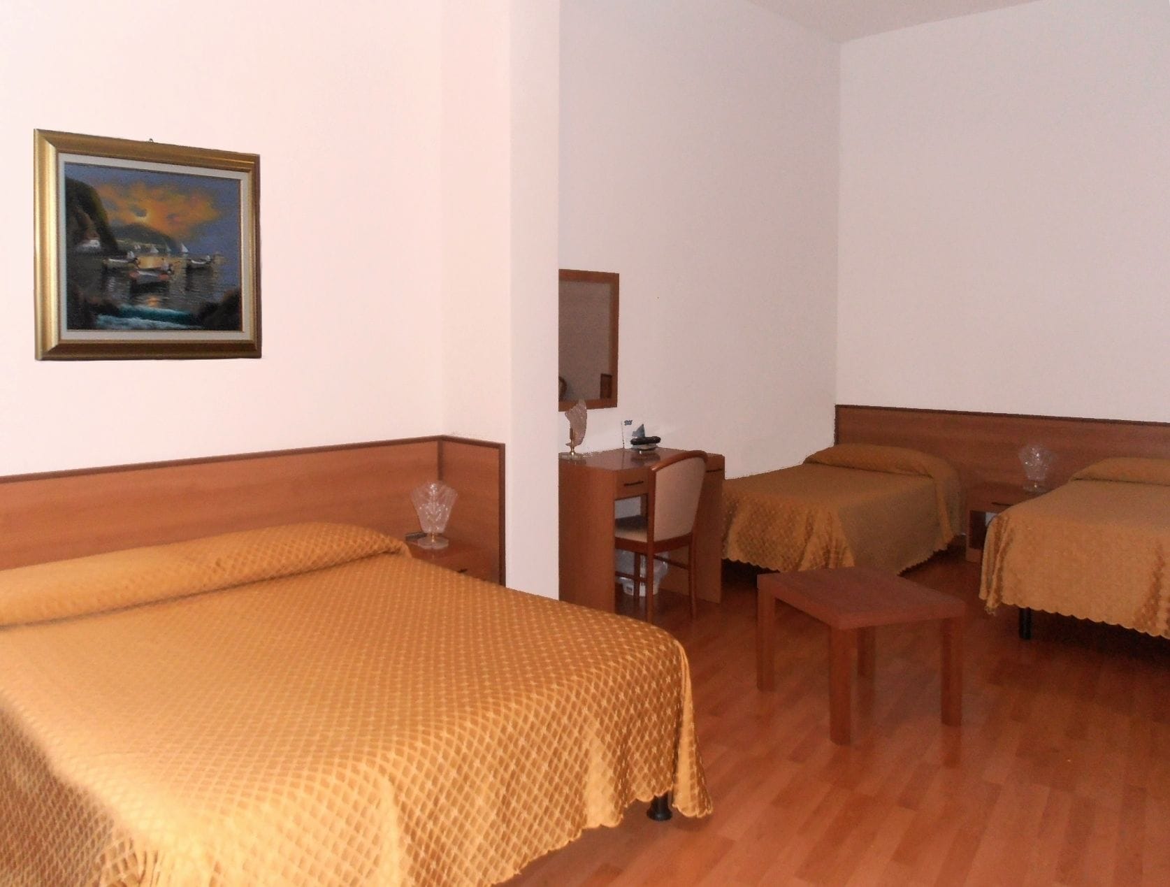 Ein Hotelzimmer mit drei Betten, einem Schreibtisch und einem Stuhl.