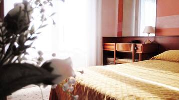 A hotel room with a bed, a desk, a chair, a lamp, and a window with curtains.