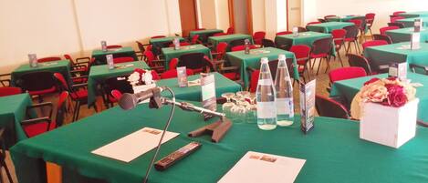 A conference room with green tables, red chairs, microphones, water bottles, and informational pamphlets.
