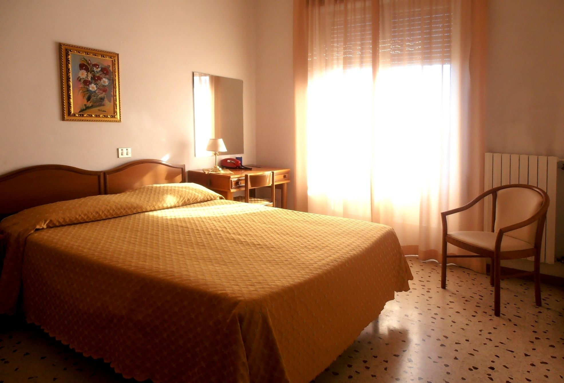 Habitación de hotel con cama, escritorio, silla, lámpara, teléfono y ventana con cortinas.
