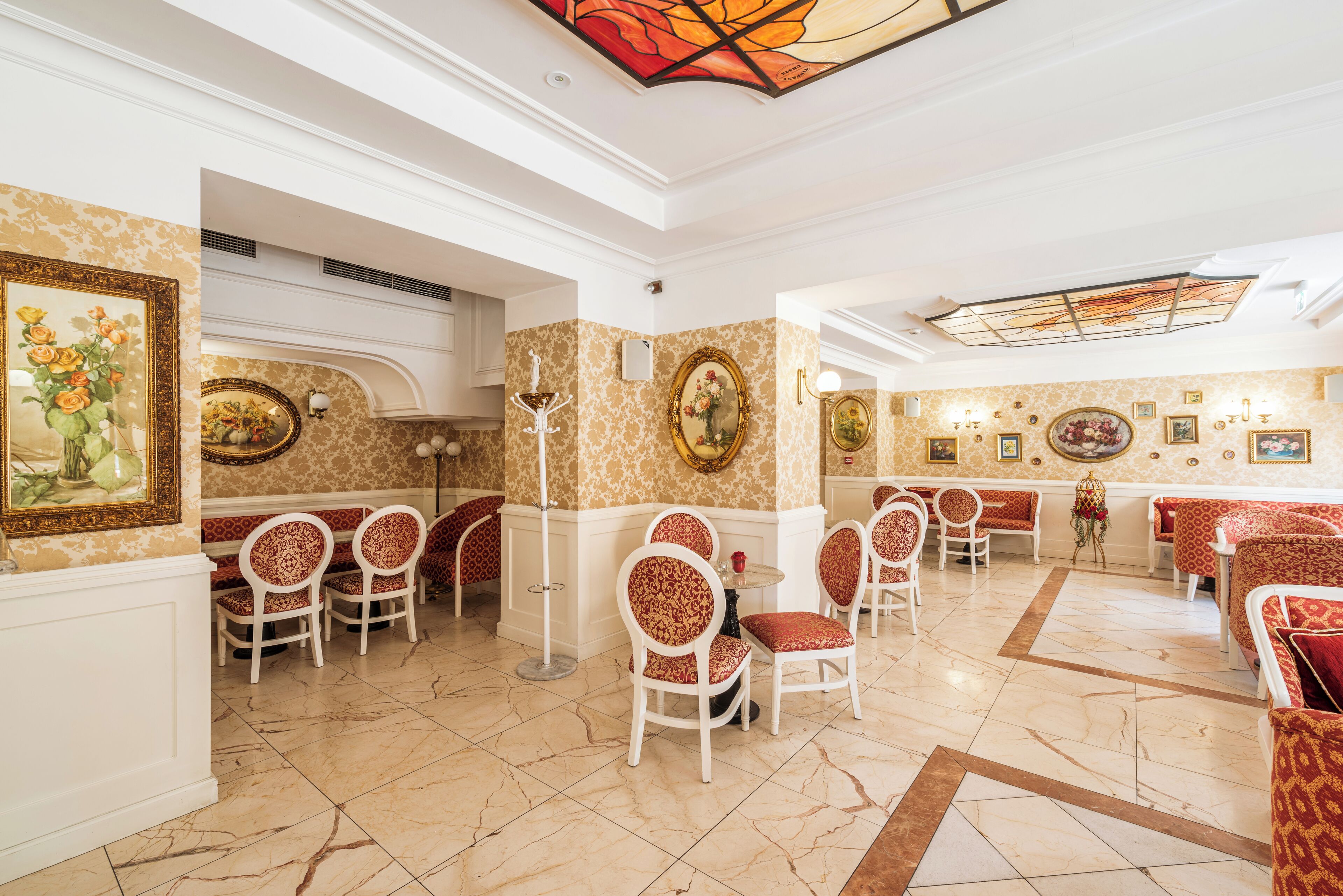 A hotel lobby with marble flooring, red and white patterned chairs, and framed artwork on the walls.