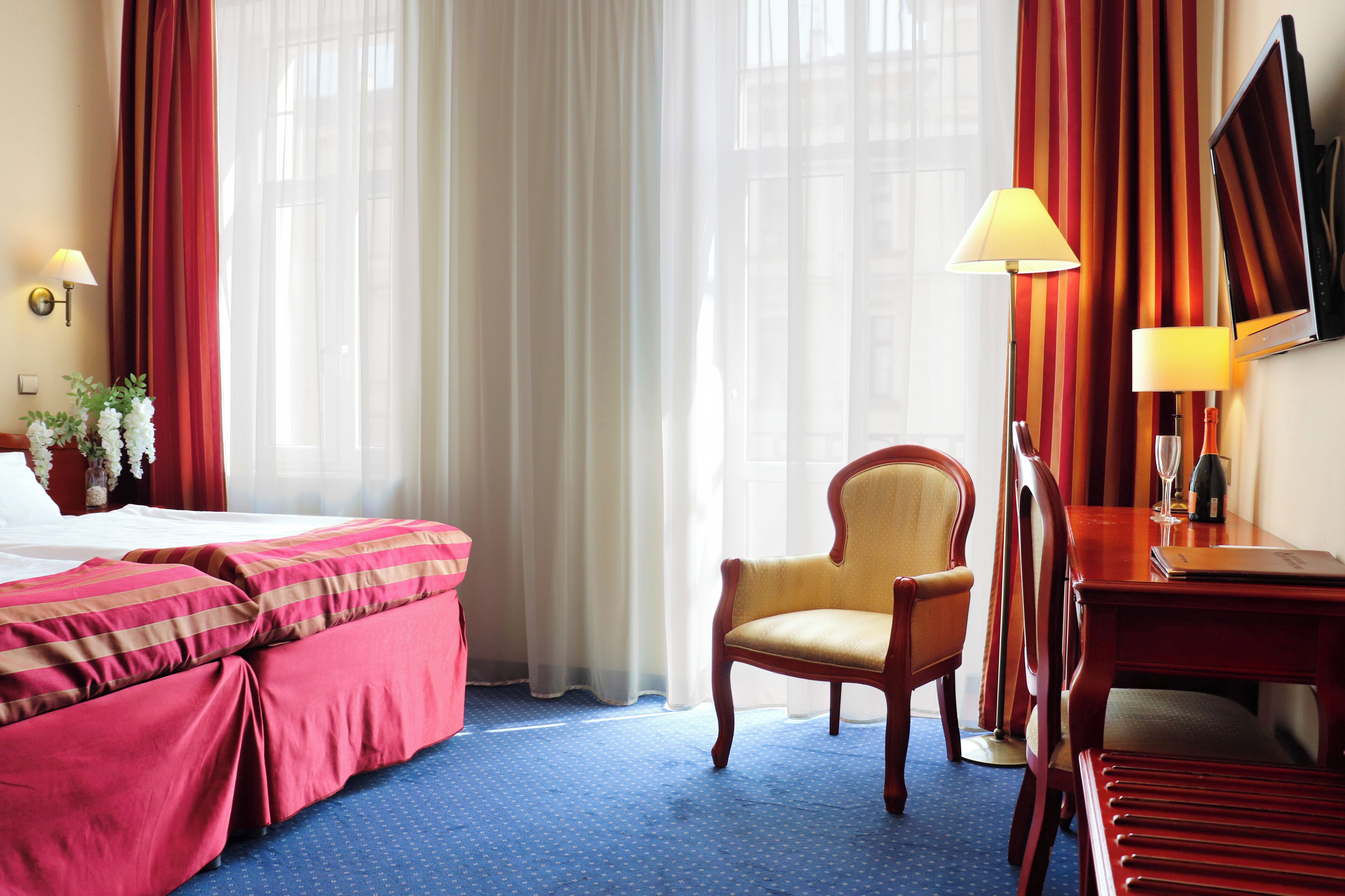 Una habitación de hotel con cama, una silla, un escritorio, una lámpara y un televisor.
