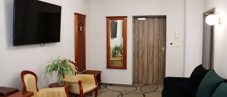 A living room with a flat-screen TV, two wooden chairs, a sofa, a mirror, and a door.