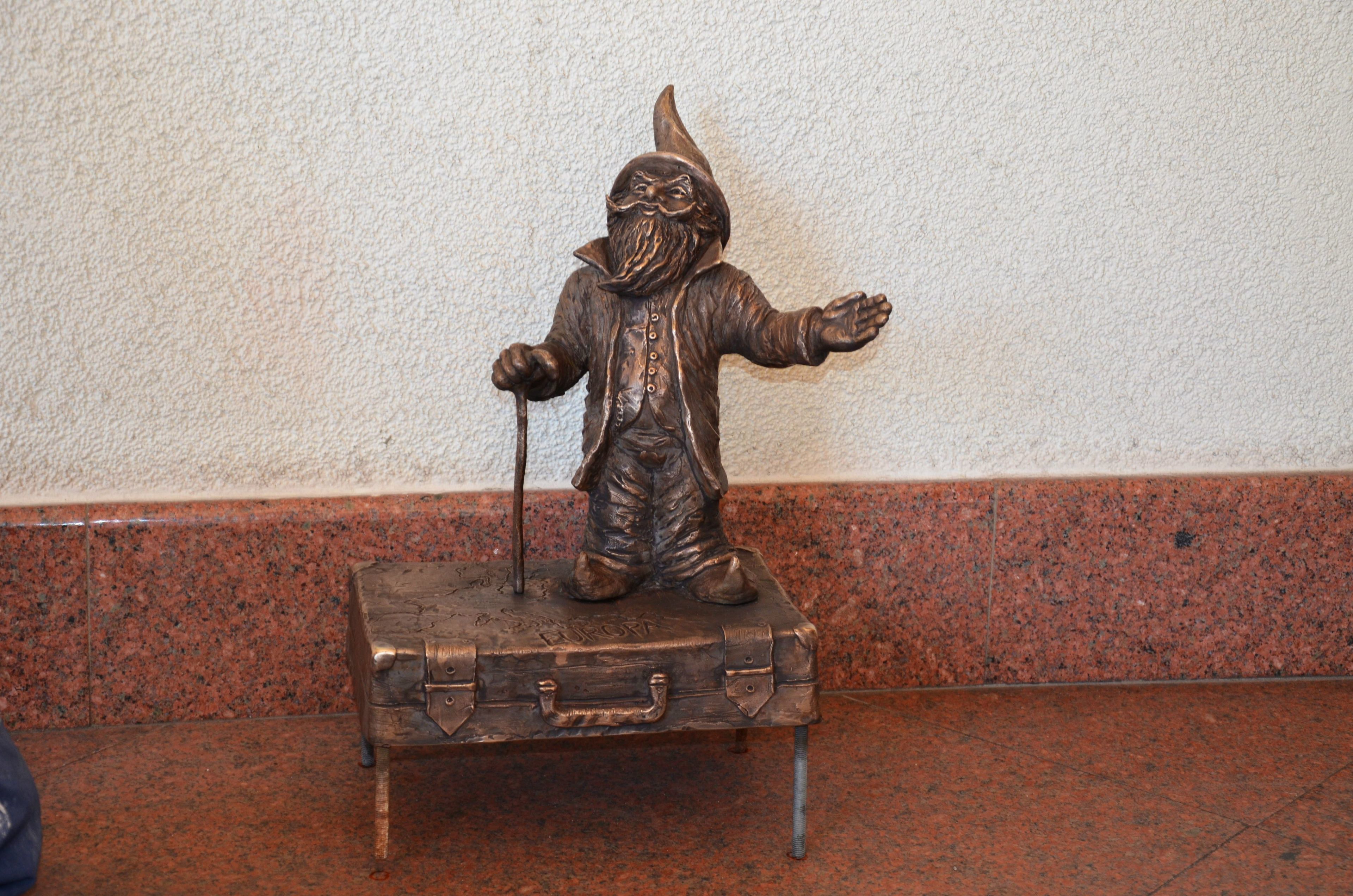 A bronze statue of a figure with a hat and cane standing on a suitcase.