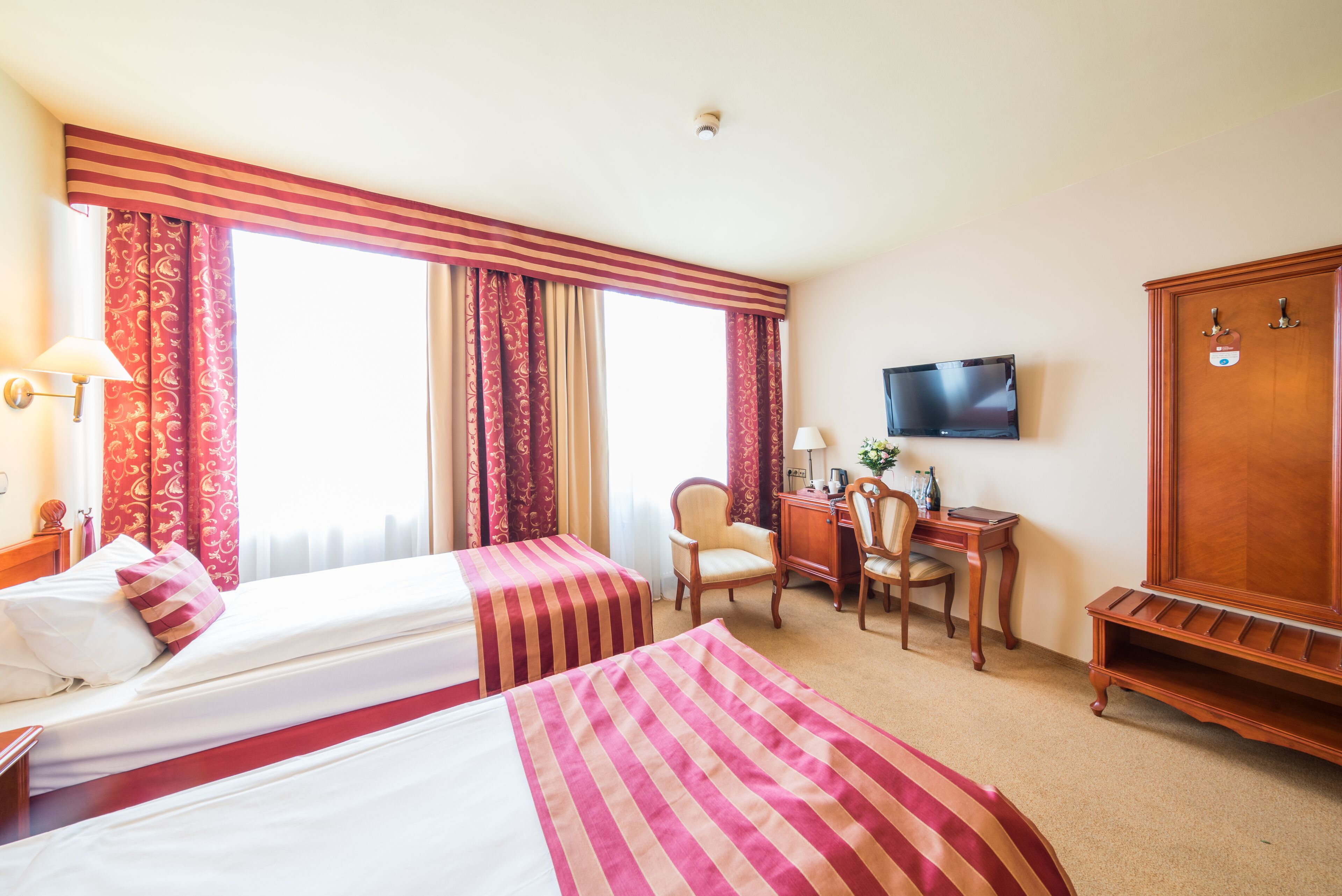 Une chambre d’hôtel avec deux lits, un bureau avec une chaise, une télévision et une armoire.