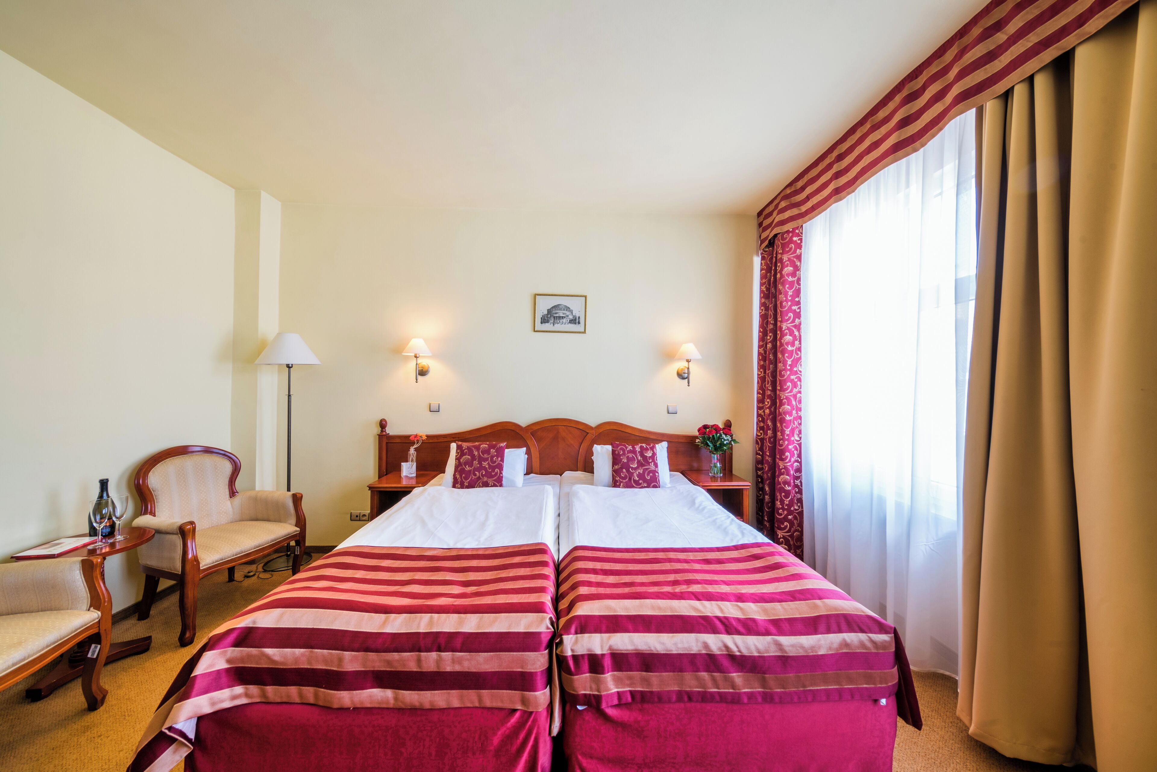 A hotel room with two beds, a chair, a nightstand, and a lamp.