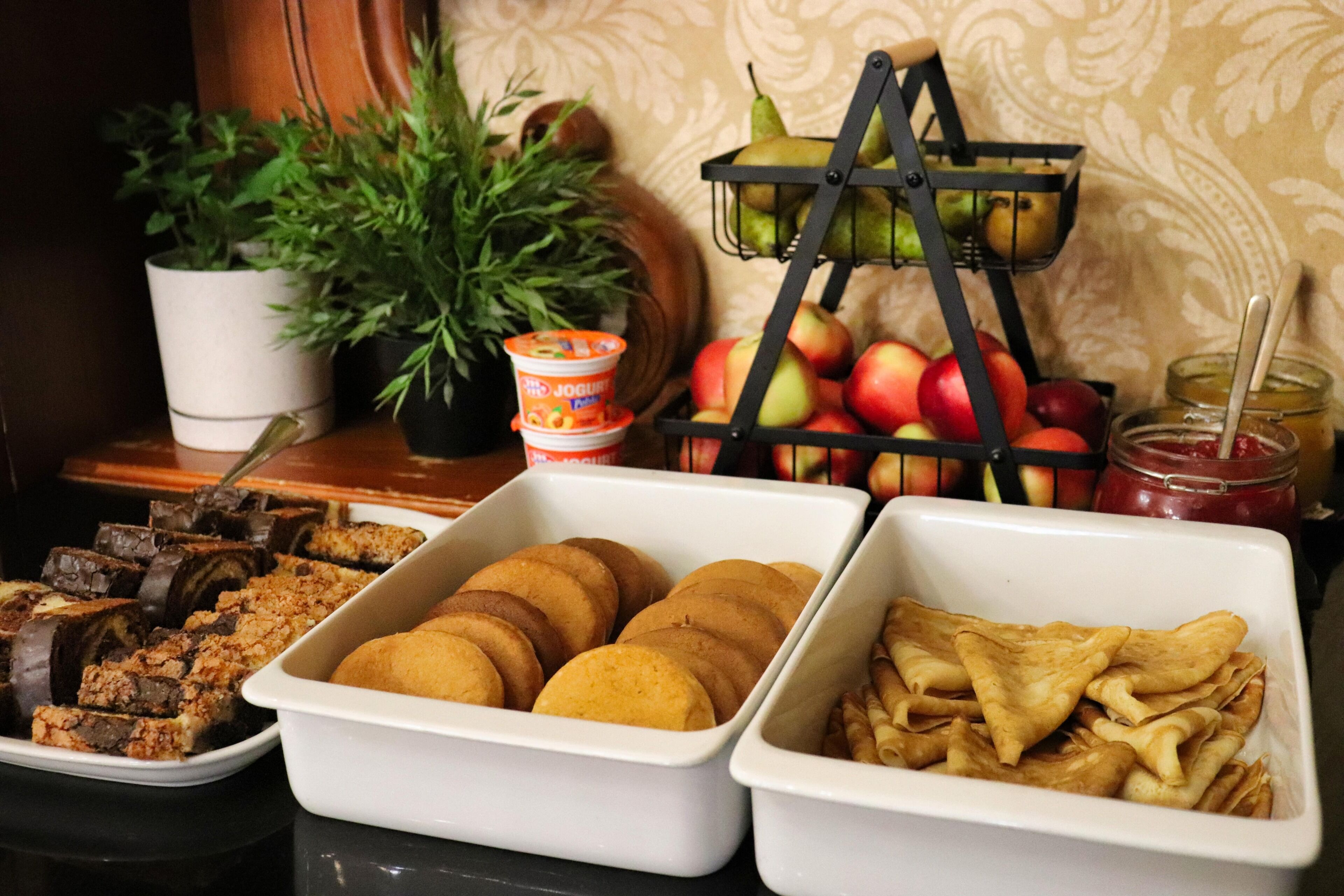 Una mesa de buffet con diversas opciones de comida, incluyendo pasteles, frutas y una cesta de frutas.