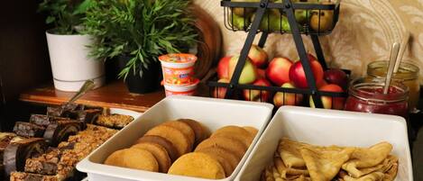 Una mesa de buffet con diversas opciones de comida, incluyendo pasteles, frutas y una cesta de frutas.