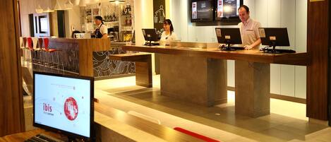 A hotel reception area with multiple computer monitors, a reception desk, and a seating area with chairs.