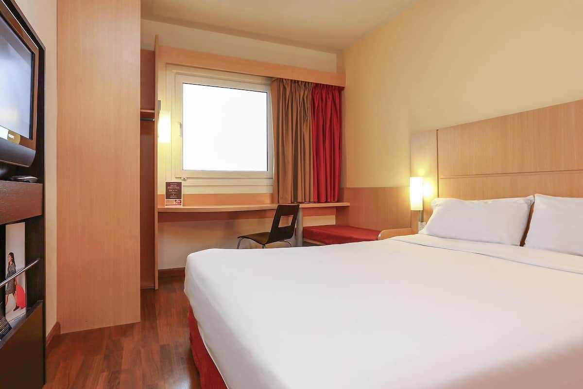 A hotel room with a bed, a desk, a chair, and a television.