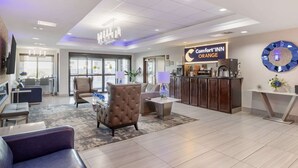 A modern hotel lobby with a reception desk, seating area, and a large clock on the wall. - Comfort Inn Orange I-10 (Orange)