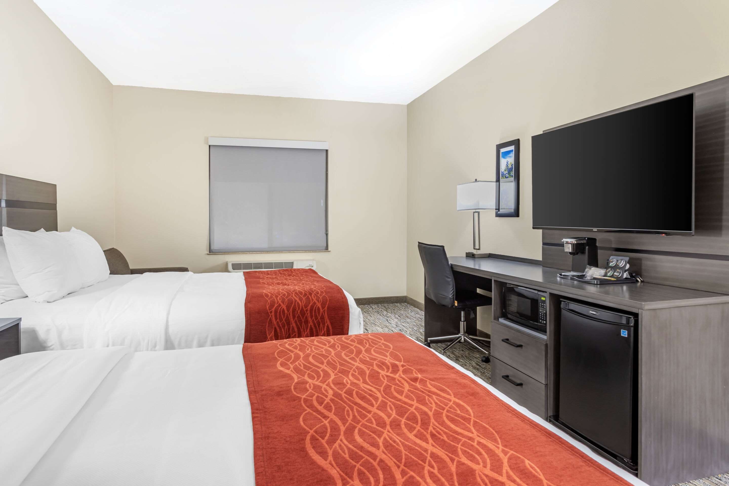 A hotel room with two beds, a desk, a television, and a microwave.