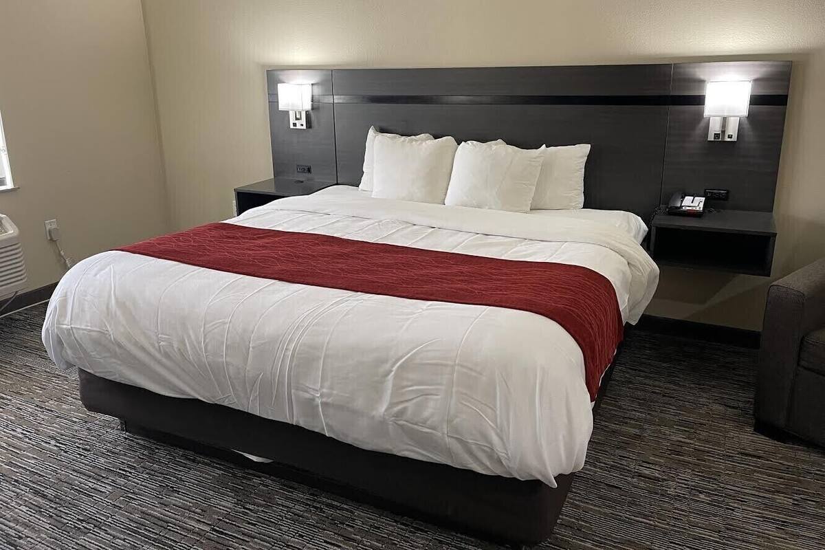 A hotel room with a large bed, two bedside tables, and a headboard with built-in lighting.