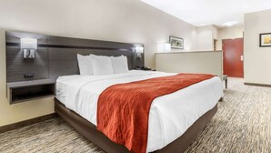 A hotel room with a large bed, a nightstand, a wall-mounted lamp, and a door. - Comfort Inn Orange I-10 (Orange)