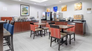 A modern hotel dining area with wooden tables and chairs, a coffee machine, and a refrigerator.