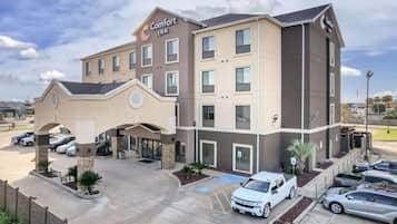 A Comfort Inn hotel with a central entrance, multiple parking spaces, and a clear sky.