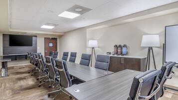 A conference room with a long table, multiple chairs, a TV screen, and two lamps.