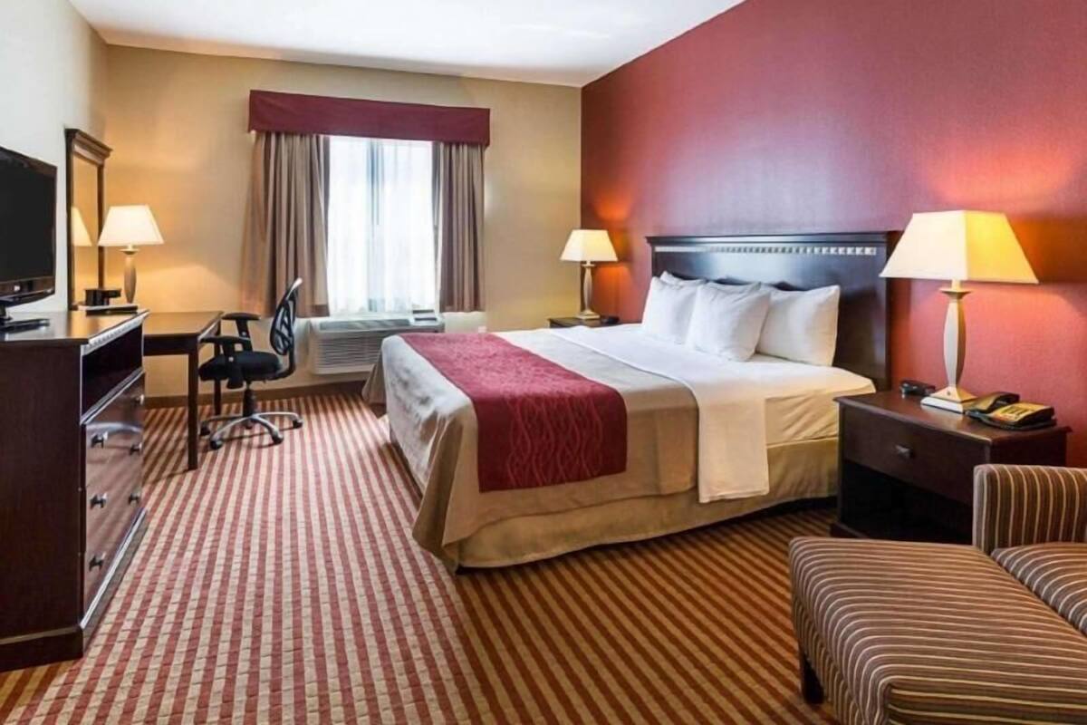 A hotel room with a bed, bedside tables, a desk with a chair, a television, and a window with curtains.