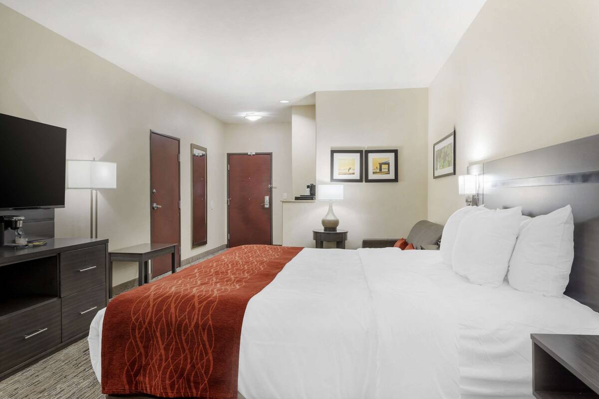 A hotel room with a large bed, a desk, a chair, a television, and two doors.