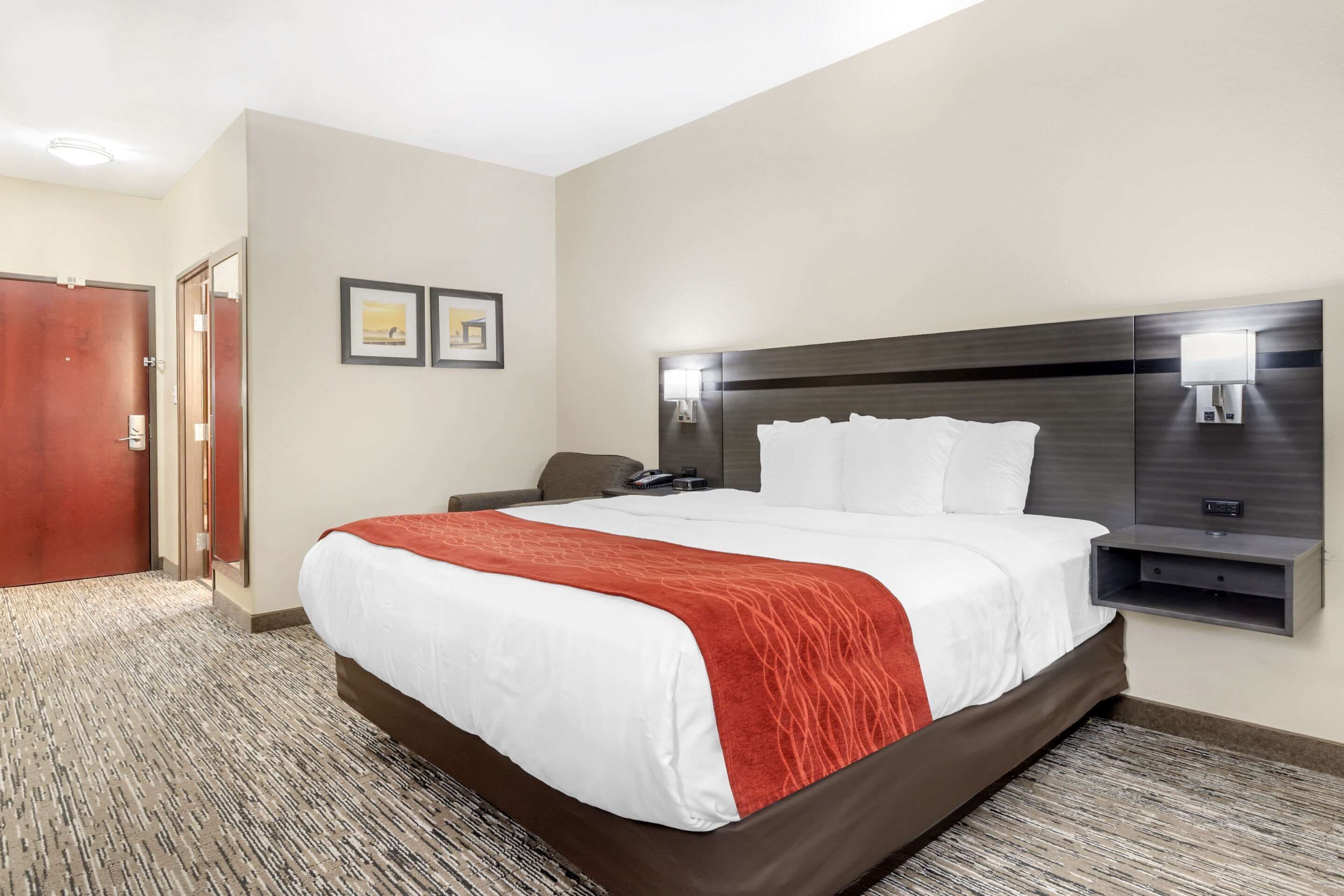 A hotel room with a large bed, a headboard with lights, a desk, and a chair.