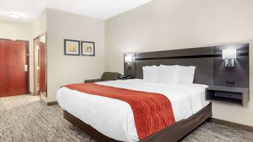 A hotel room with a large bed, a headboard with lights, a desk, and a chair.