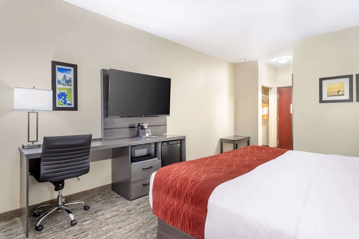 A hotel room with a bed, desk, chair, television, and artwork on the walls.