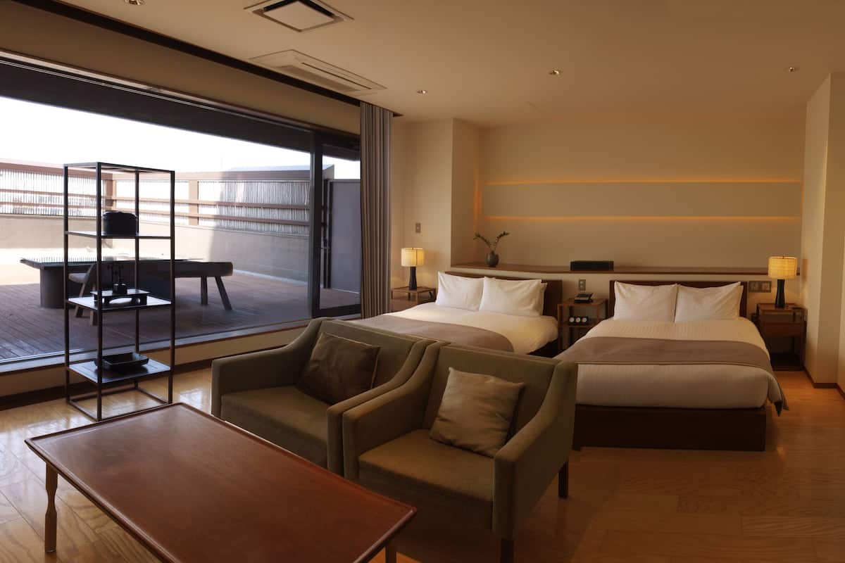 A hotel room with two beds, a sofa, a table, and a balcony with a table and chairs.