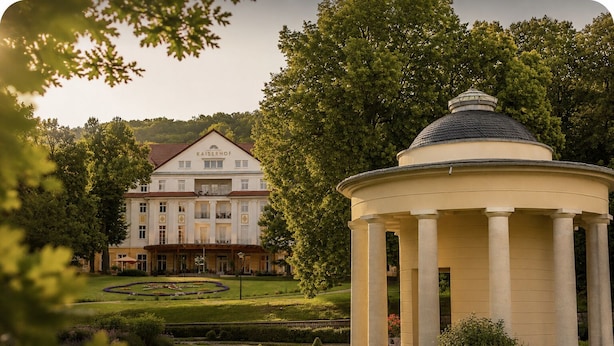 A classical building with a central dome and a symmetrical facade, surrounded by a well-manicured garden. - Kulturhotel Kaiserhof (Bad Liebenstein)