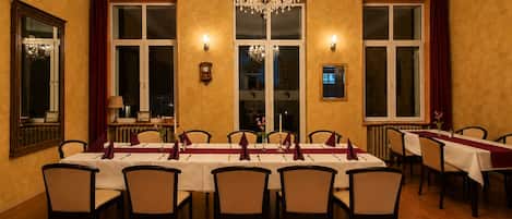 A dining room with a long table set for six, surrounded by chairs, with a chandelier above.