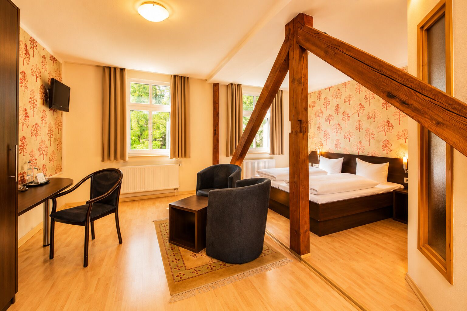Una habitación de hotel con cama, escritorio, silla, televisor y ventana con cortinas.