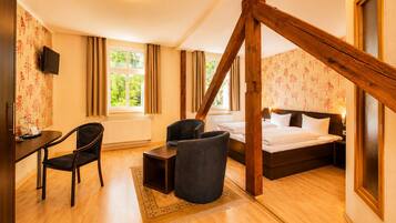 Una habitación de hotel con cama, escritorio, silla, televisor y ventana con cortinas.