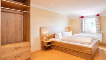 Een slaapkamer met een houten bed, een nachtkastje met een lamp, een houten garderobe en een raam met gordijnen.