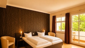 A hotel room with a large bed, two bedside tables, a chair, and a window with a view of greenery. - Kulturhotel Kaiserhof (Bad Liebenstein)