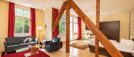 Una sala moderna con techo de vigas de madera, un sofá, sillones, una mesa de centro de vidrio y una cama con cabecera de madera.