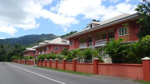 Una hilera de edificios coloniales rojos con balcones, rodeados de exuberante vegetación y una montaña al fondo.