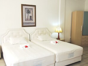 A hotel room with two beds, a nightstand with a lamp, a wardrobe, and a framed picture on the wall.