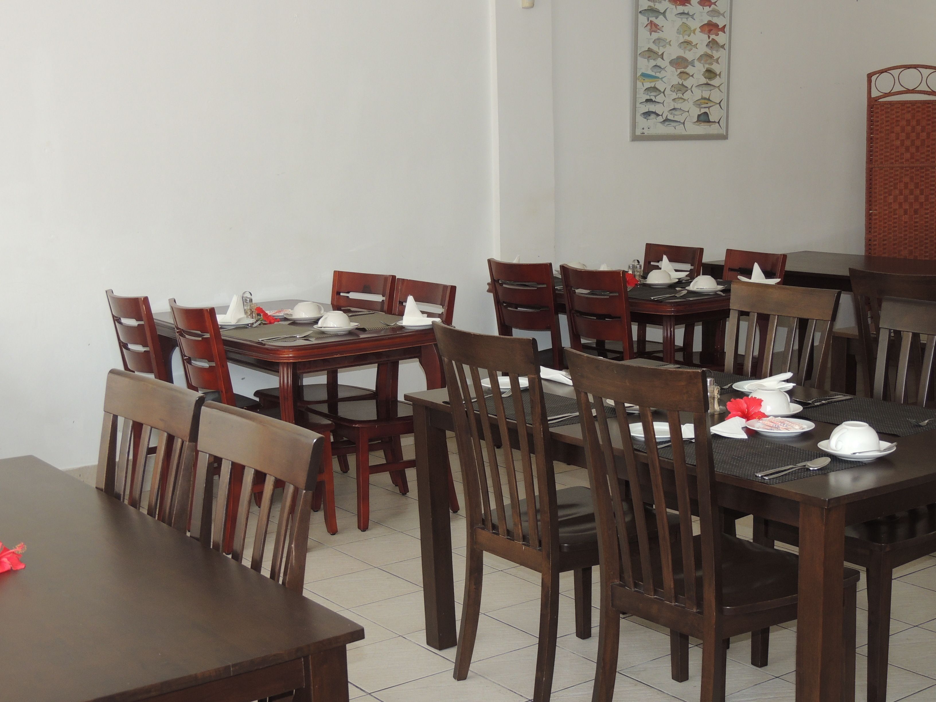A dining area with wooden tables and chairs, white tablecloths, and neatly arranged table settings.