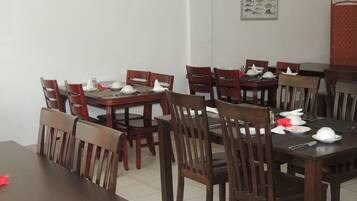 A dining area with wooden tables and chairs, white tablecloths, and neatly arranged table settings.