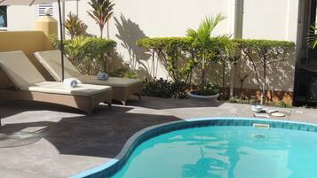 Una piscina al aire libre, sombrillas, sillones reclinables de piscina