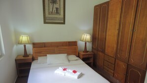 Una cama bien hecha con sábanas blancas, dos lámparas de noche, un cabecero de madera y un amplio armario de madera.