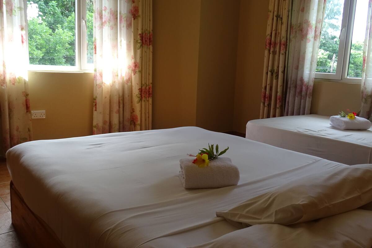 A hotel room with two beds, floral curtains, and a view of greenery outside.