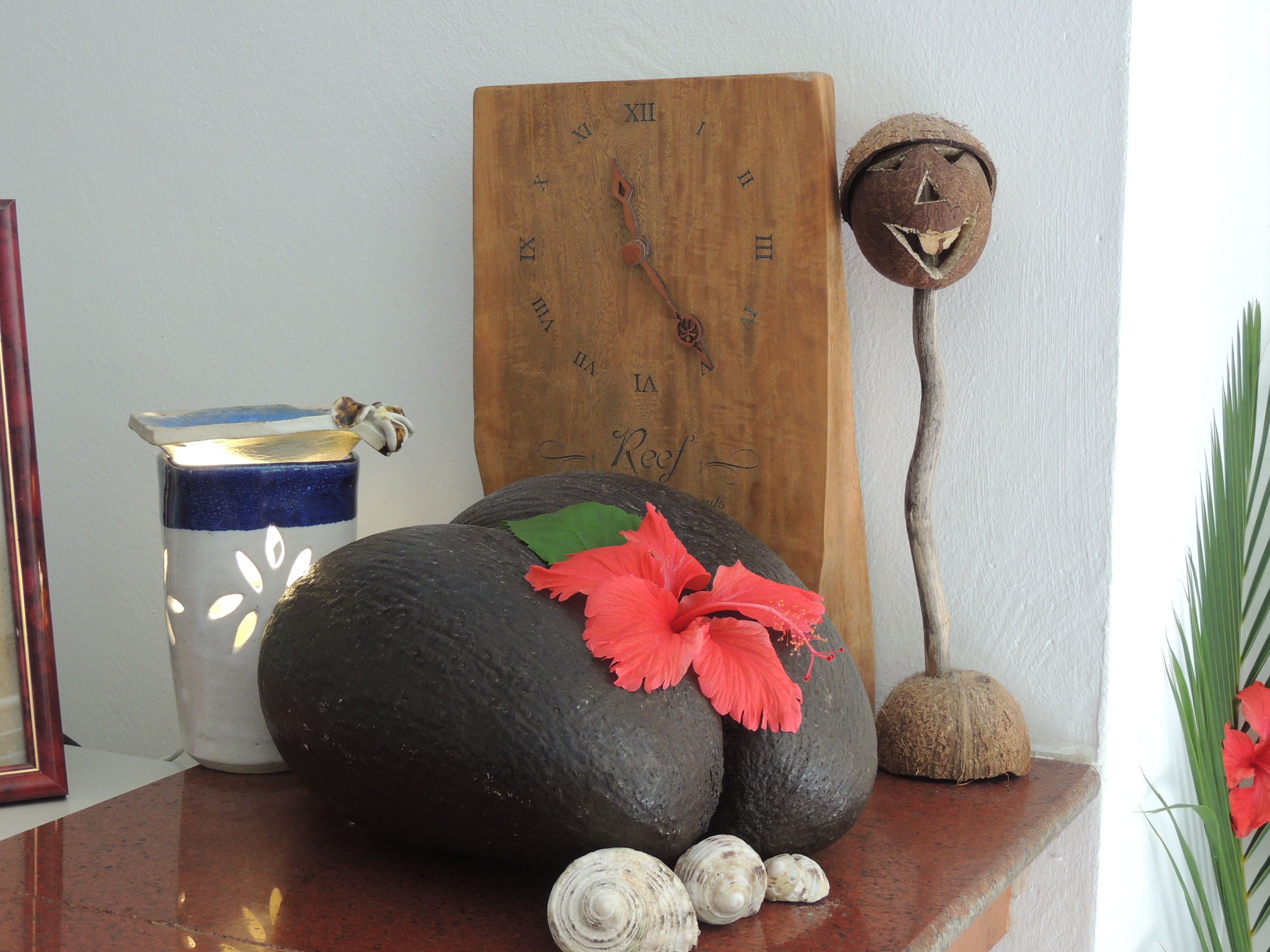 A wooden clock with Roman numerals, a rustic decoration resembling a face, and a vase with a blue and white pattern.