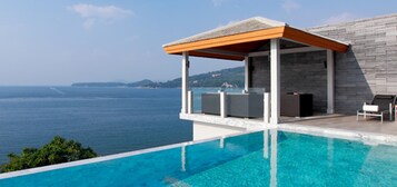 Una piscina infinita moderna con vistas despejadas al mar, un área de estar cubierta con fachada de piedra y una tumbona.